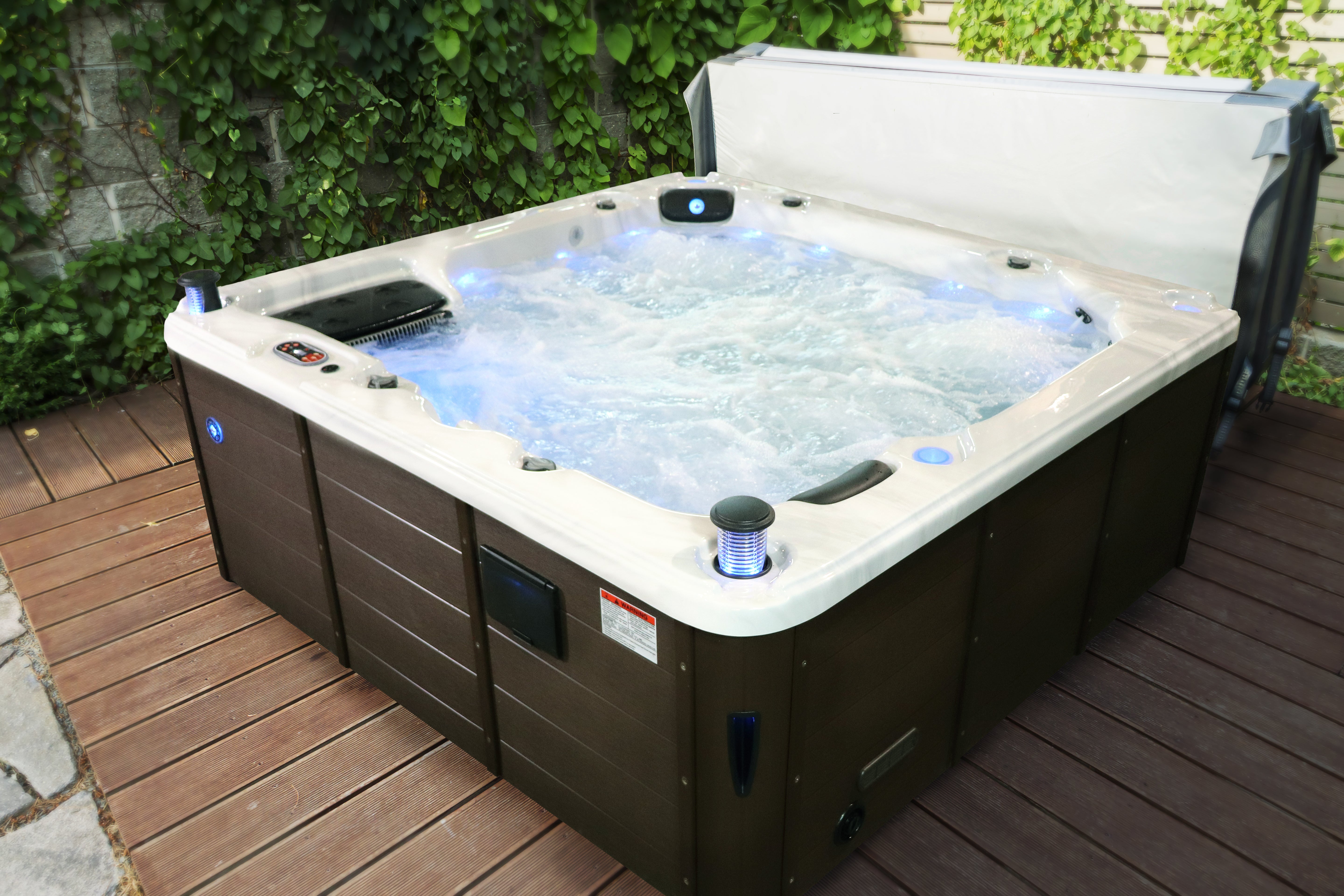 Thunder Bay 6-person outdoor hot tub on a garden deck with the hardtop cover open, 44 hydrotherapy jets running and integrated LED lighting in the water